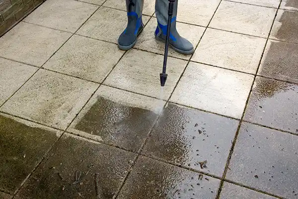 Worker in rubber boots power washing an exterior floor