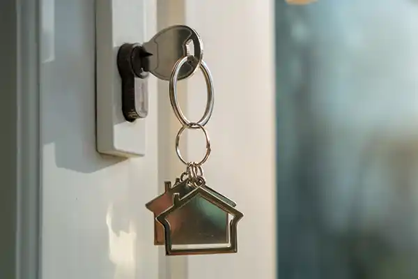 Close up of a key in a door lock with a keychain of a house hanging from it